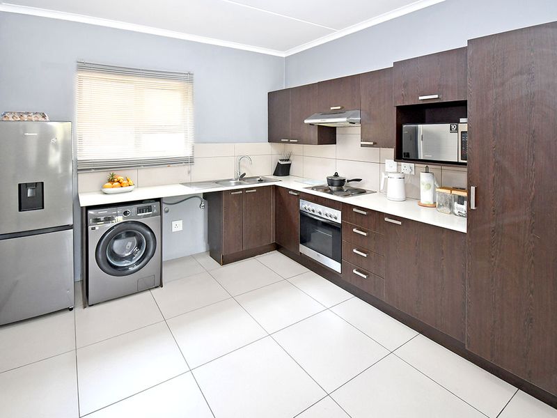 Modern kitchen featuring dark wood cabinetry, light countertops, tiled flooring, and integrated appliances including an oven and extractor fan.