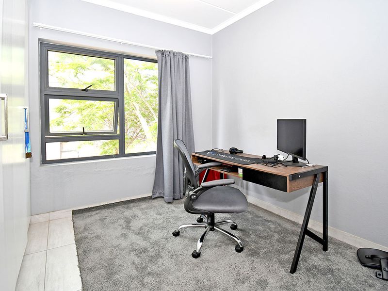 A functional bedroom featuring neutral grey walls, carpeted flooring, and a built-in wardrobe, offering a clean and versatile space.