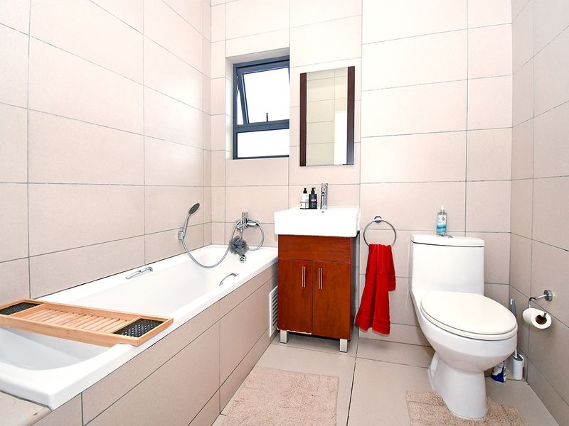 A clean, modern bathroom featuring full-height wall tiling, a built-in bathtub, a vanity cabinet with a basin, and a standard toilet.