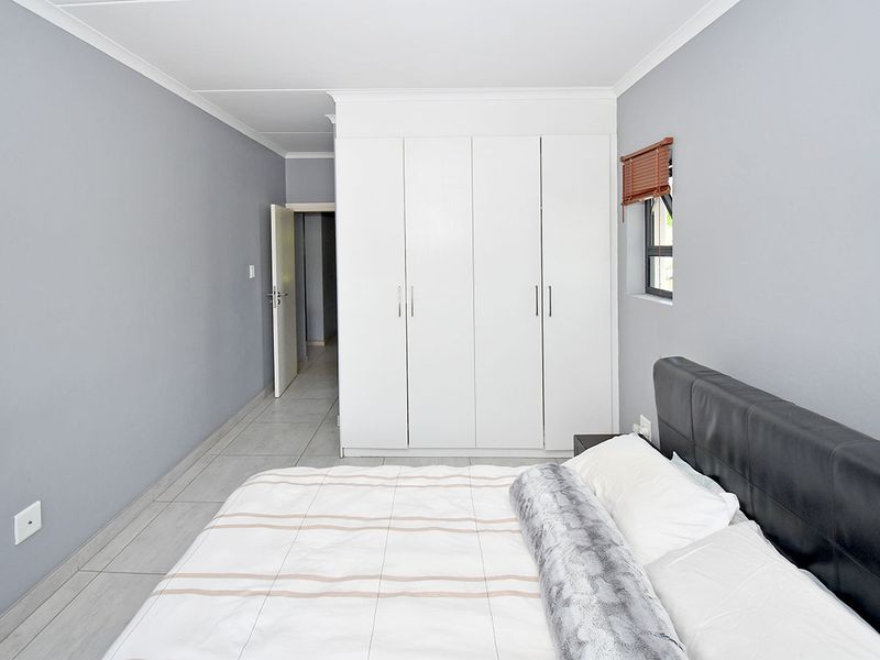 A well-maintained bedroom featuring neutral grey walls, tiled flooring, and a large white built-in wardrobe providing ample storage space.