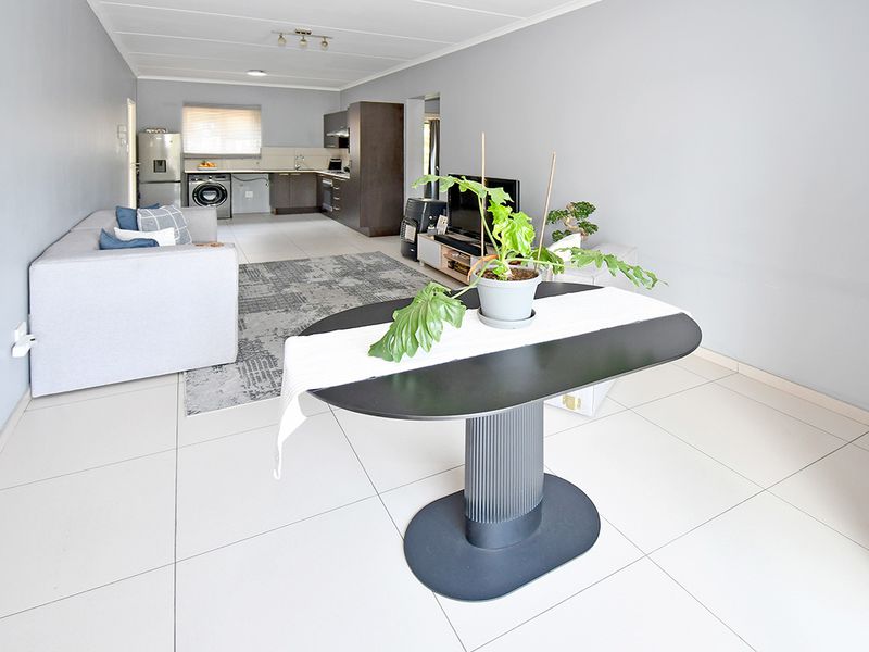 An open-plan living and kitchen area featuring neutral tiled flooring, modern dark kitchen cabinetry, and a functional layout suitable for contemporary apartment living.