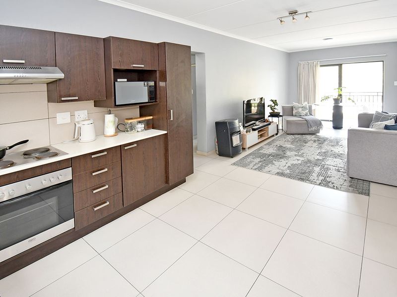 Open-plan living area featuring a modern kitchen with dark wood cabinetry, integrated appliances, and tiled flooring, leading to a bright lounge with balcony access.