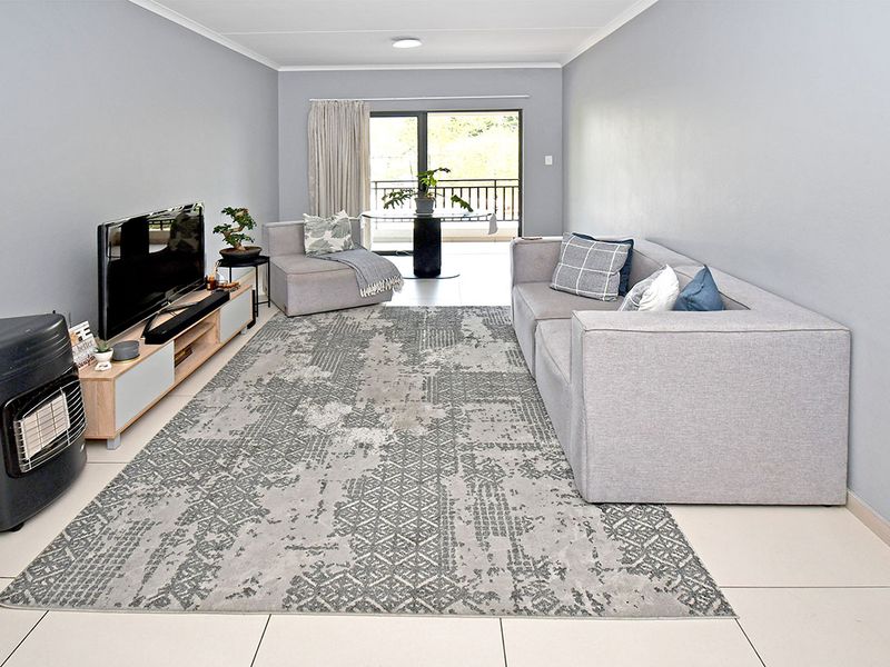 A bright, open-plan living room featuring neutral tiled flooring, smooth grey walls, and a sliding glass door providing direct access to a private balcony.