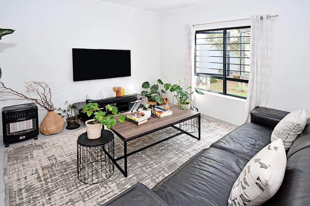 A bright and comfortable living room featuring large windows with security bars, neutral walls, and tiled flooring.
