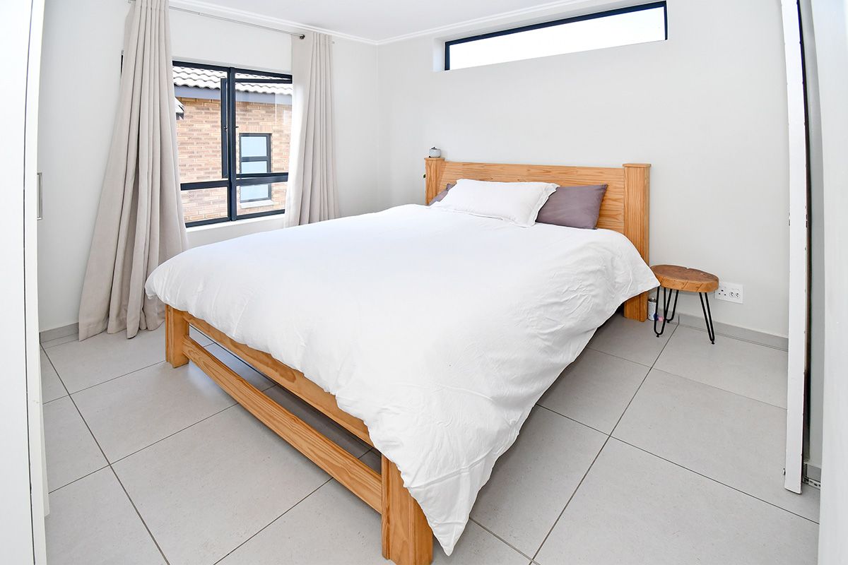 A bright bedroom featuring large format floor tiles, a clerestory window, and a standard window with curtain tracks.
