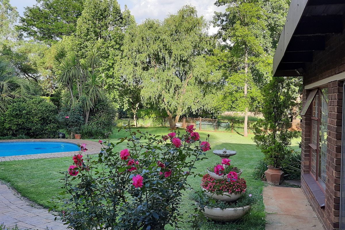 A view of the rear garden featuring a swimming pool, paved patio area, and established trees, viewed from the side of the brick dwelling.