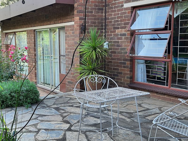 A paved patio area featuring a brick exterior facade, large sliding glass doors, and security-barred windows overlooking the garden.