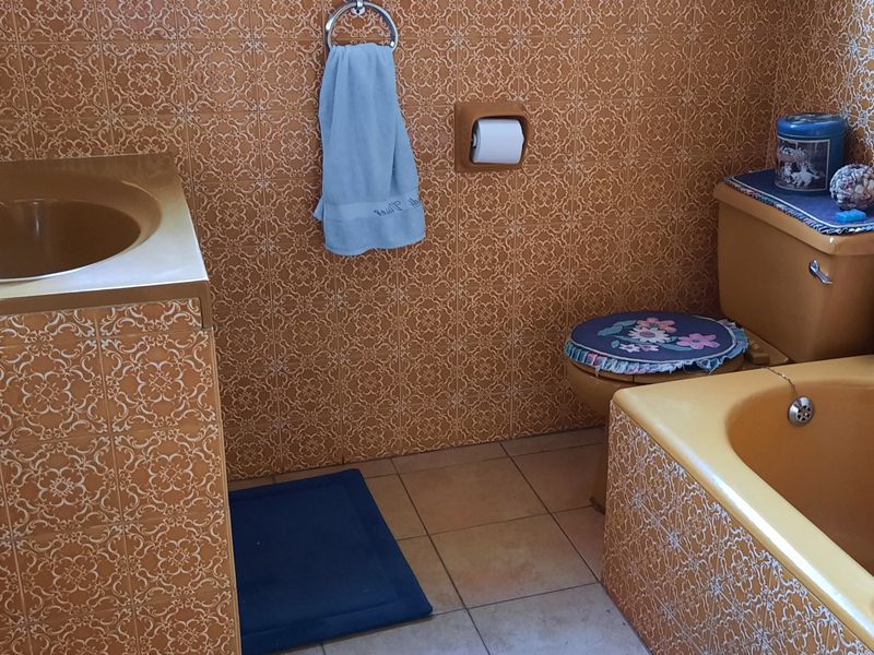 A dated bathroom featuring vintage mustard-colored sanitary ware and matching patterned wall tiles, offering a classic retro aesthetic in need of modernization.
