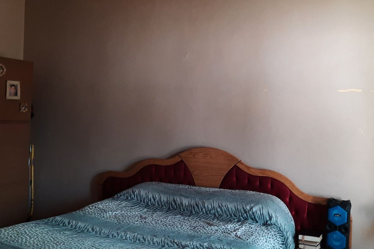 A bedroom featuring a large bed and built-in storage unit, requiring minor cosmetic updates to the wall finishes.