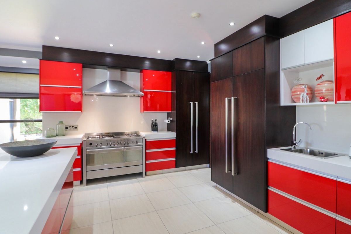 Modern kitchen featuring high-gloss red and dark wood cabinetry, stone countertops, stainless steel gas range, extractor fan, and integrated refrigerator.