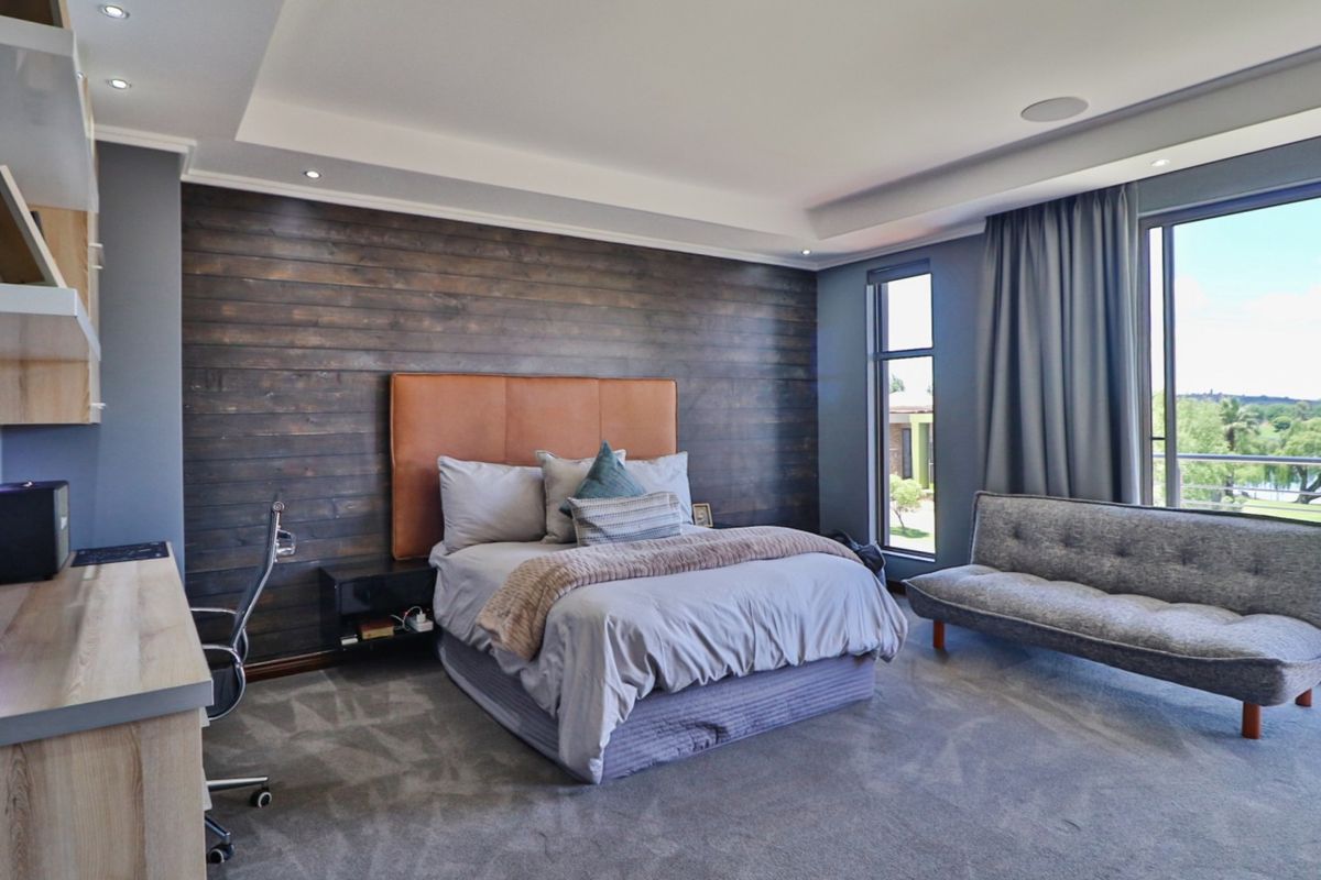 Spacious bedroom featuring a dark wood-paneled accent wall, recessed ceiling lighting, built-in desk cabinetry, and large windows with views.
