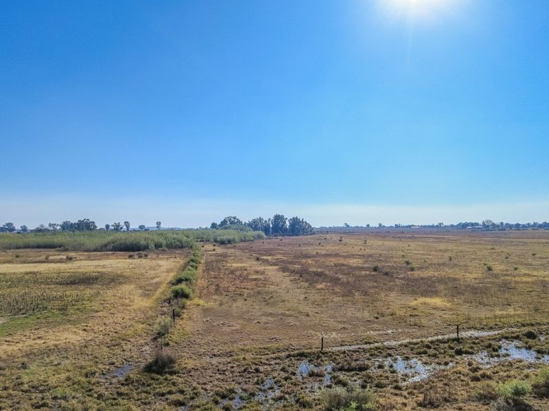 An expansive view of the open small holding landscape featuring natural vegetation and perimeter fencing under a clear blue sky.