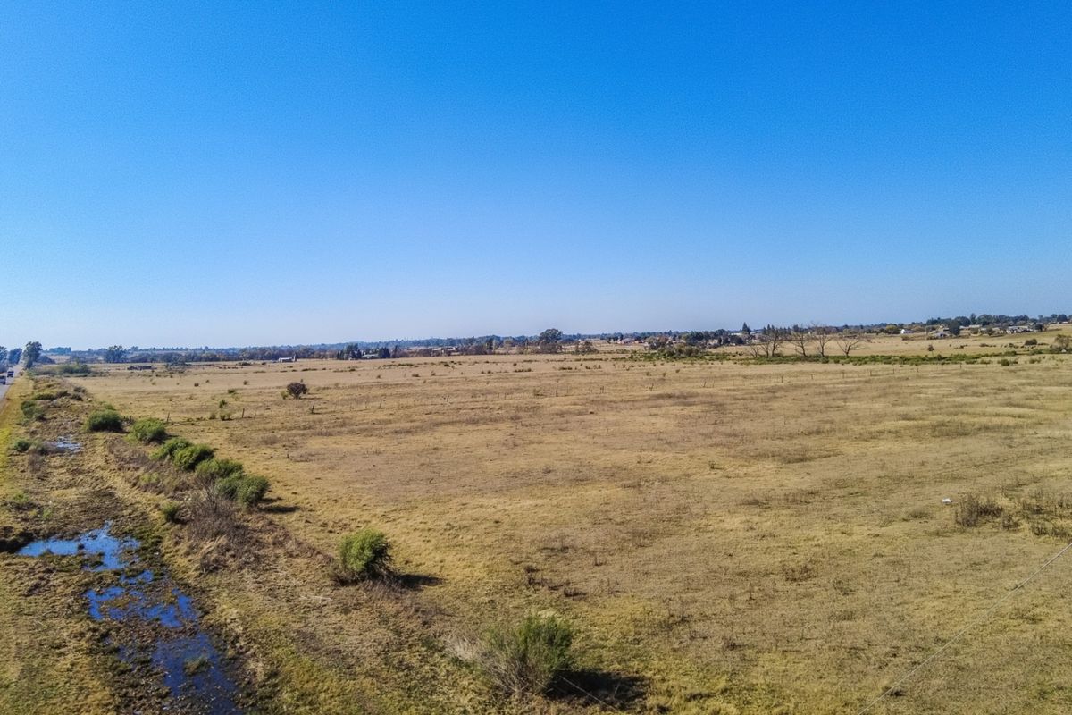 An aerial view of a large, open field on a small holding, featuring natural vegetation and boundary fencing under a clear blue sky.