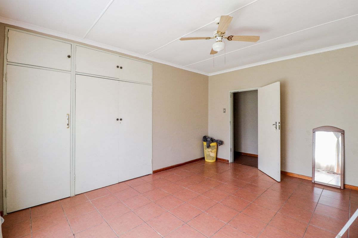 A spacious bedroom featuring built-in cupboards, tiled flooring, and a ceiling fan, offering a neutral canvas for personalization.