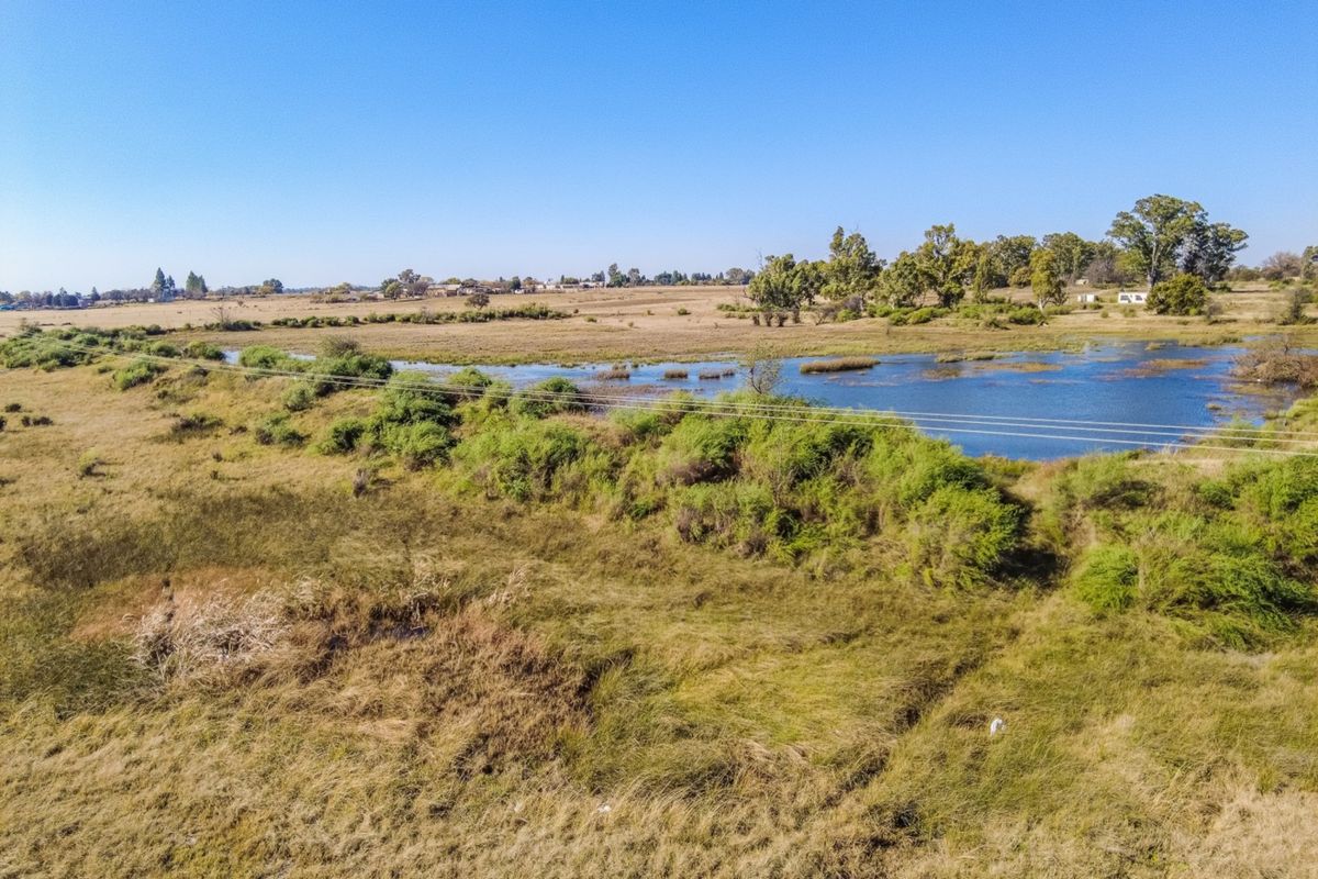 An aerial view of the small holding property featuring open grassland and a natural dam with overhead power lines crossing the landscape.