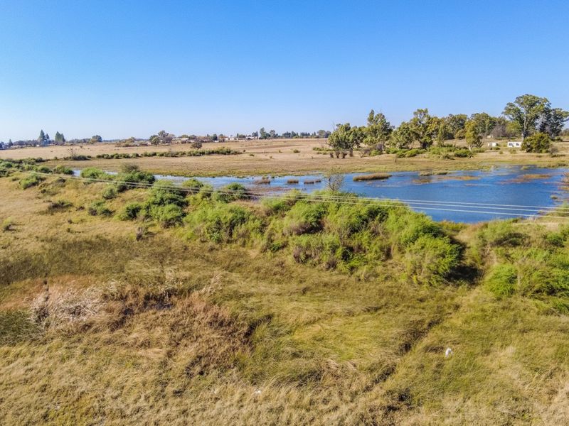 An aerial view of the small holding property featuring open grassland and a natural dam with overhead power lines crossing the landscape.