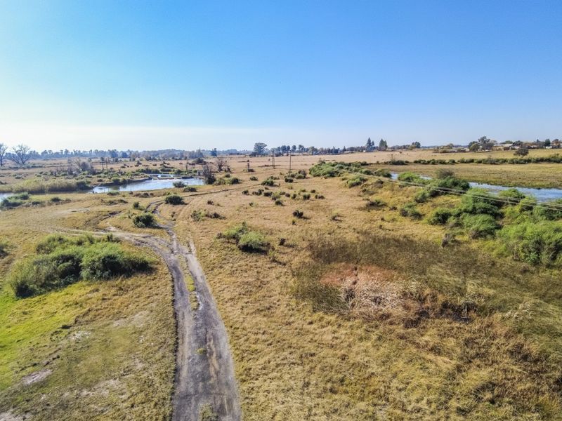 Aerial view of the small holding property featuring expansive open land, a dirt access road, and natural river frontage.
