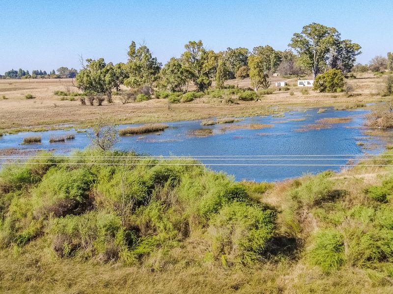 A scenic view of a natural dam surrounded by indigenous vegetation and open landscape on the small holding.