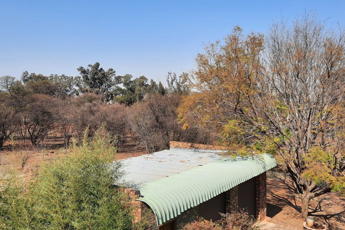 Elevated view of a small holding property featuring a brick structure with a curved corrugated metal roof set amongst mature trees and natural landscape.