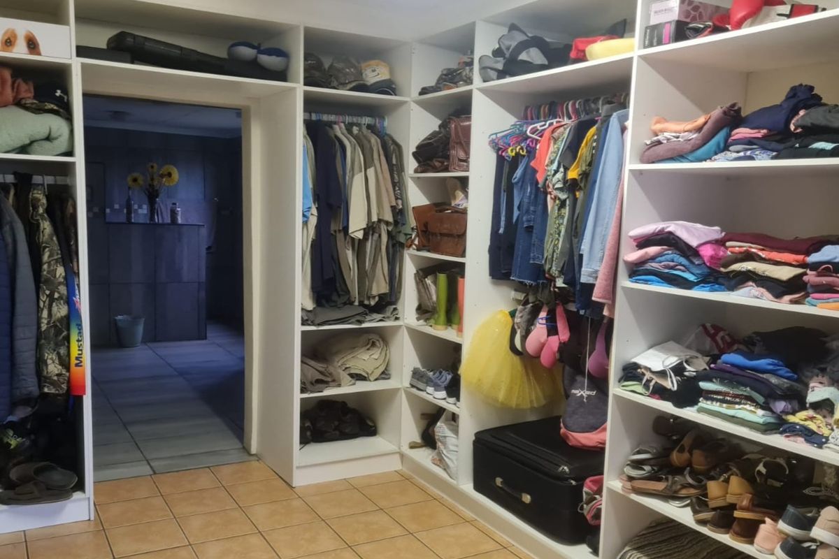 A walk-in closet or dressing area featuring extensive built-in white cabinetry with open shelving and hanging rails, finished with tiled flooring.