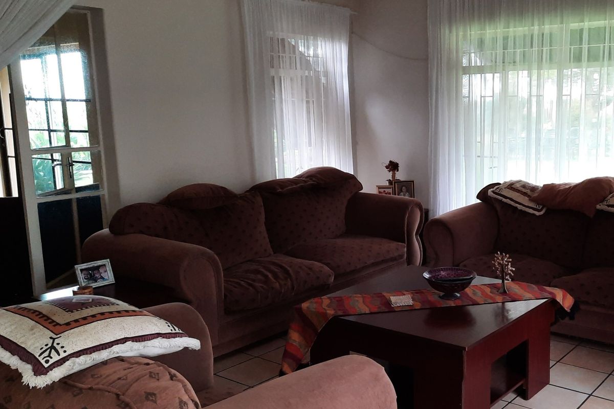 A spacious living room featuring tiled flooring and large windows that provide ample natural light, with access to an exterior glass panel door.