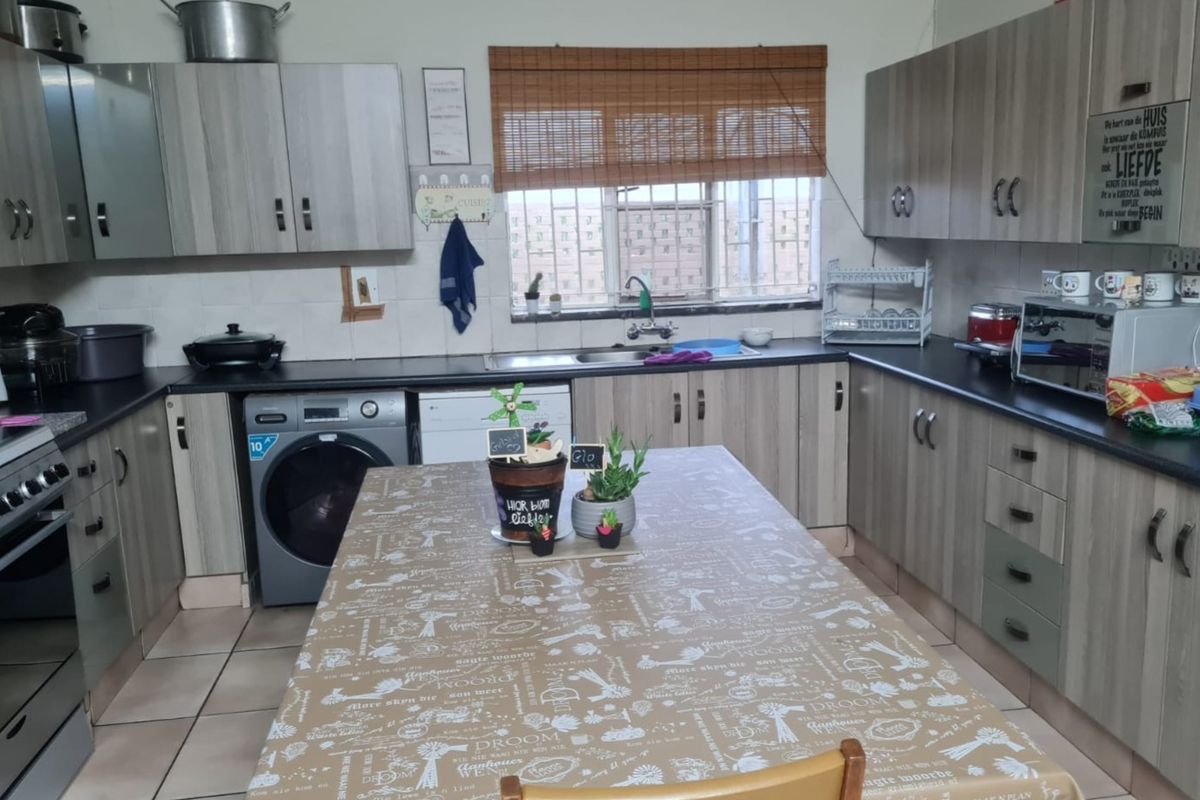 Functional kitchen featuring light wood-look cabinetry, dark laminate countertops, tiled flooring, and integrated laundry and dishwasher appliances.