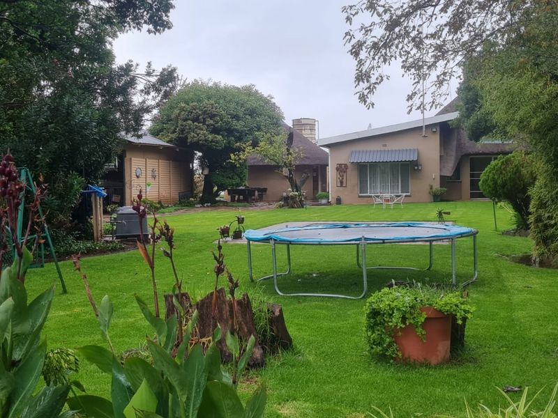 A spacious rear garden featuring a well-maintained lawn, mature trees, and a view of the main dwelling with traditional thatched roofing.