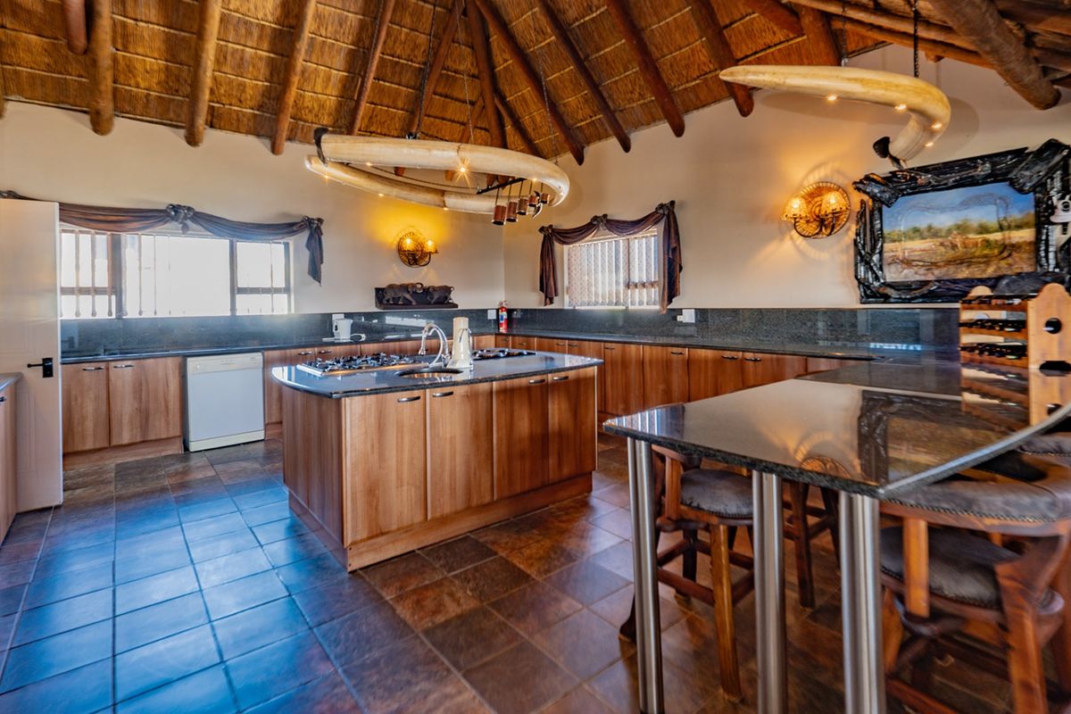 Spacious kitchen featuring a high thatched ceiling, granite countertops, a central island with a gas hob, and ample wooden cabinetry.