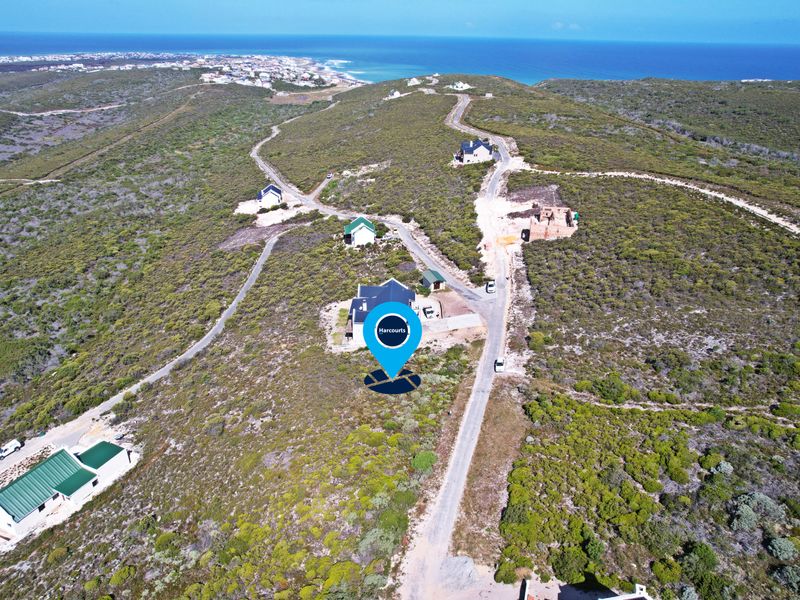 Aerial view of a vacant residential plot situated in a coastal landscape with established gravel road access and surrounding natural vegetation.