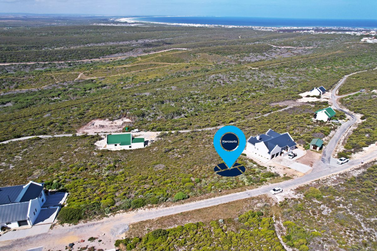 Aerial view of a vacant residential plot situated in a coastal landscape with nearby established homes and gravel road access.