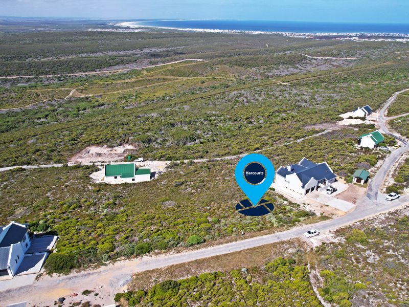 Aerial view of a vacant residential plot situated in a coastal landscape with nearby established homes and gravel road access.