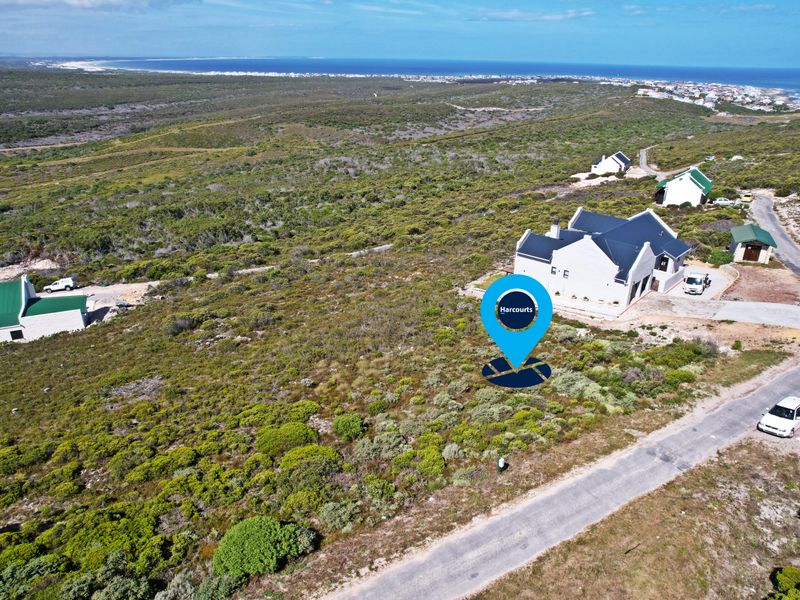 Aerial view of a vacant residential plot situated in a coastal estate, featuring natural vegetation and proximity to existing residential developments.