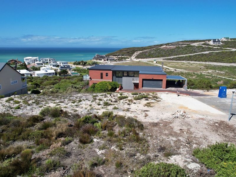 Aerial view of a modern brick residential property featuring a metal roof, garage, and carport, situated in a coastal landscape with ocean views.