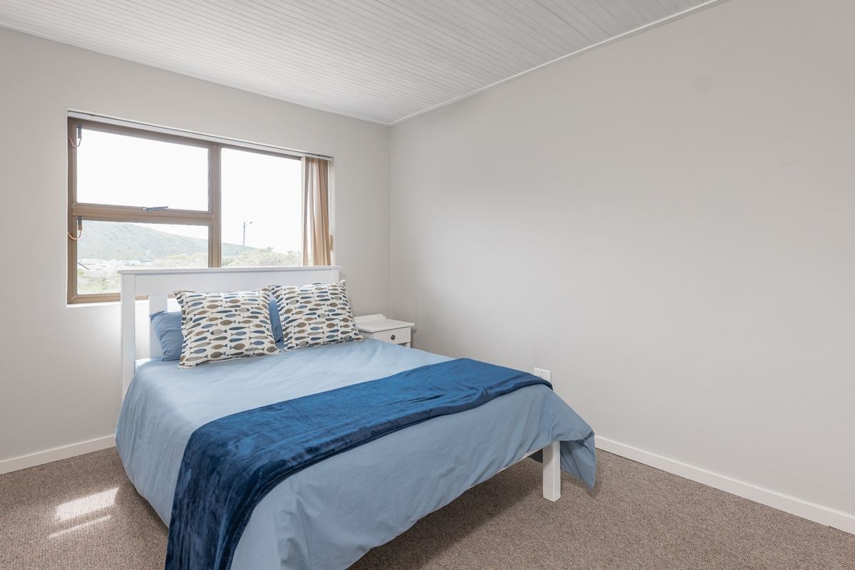 A simple bedroom featuring neutral walls, carpeted flooring, and a tongue and groove ceiling with natural light from the window.