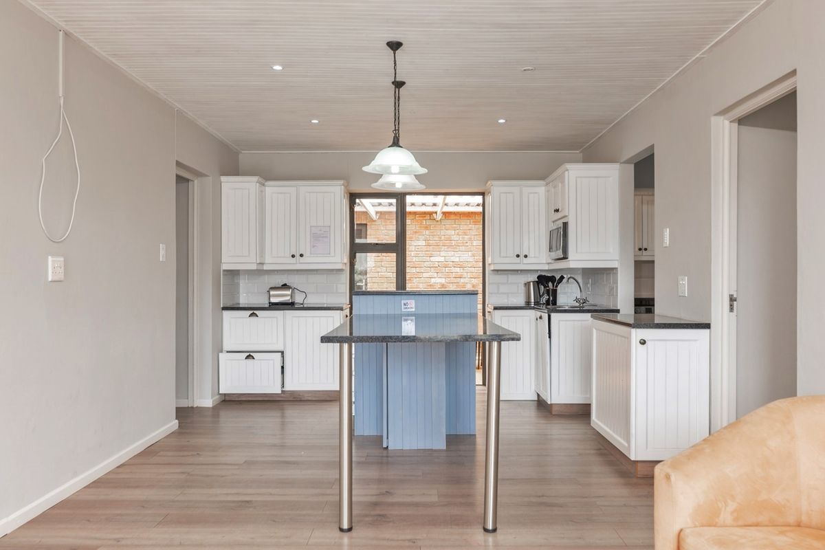 A bright, well-maintained kitchen featuring white cabinetry, dark stone countertops, a central island, and modern pendant lighting with wood-look laminate flooring.