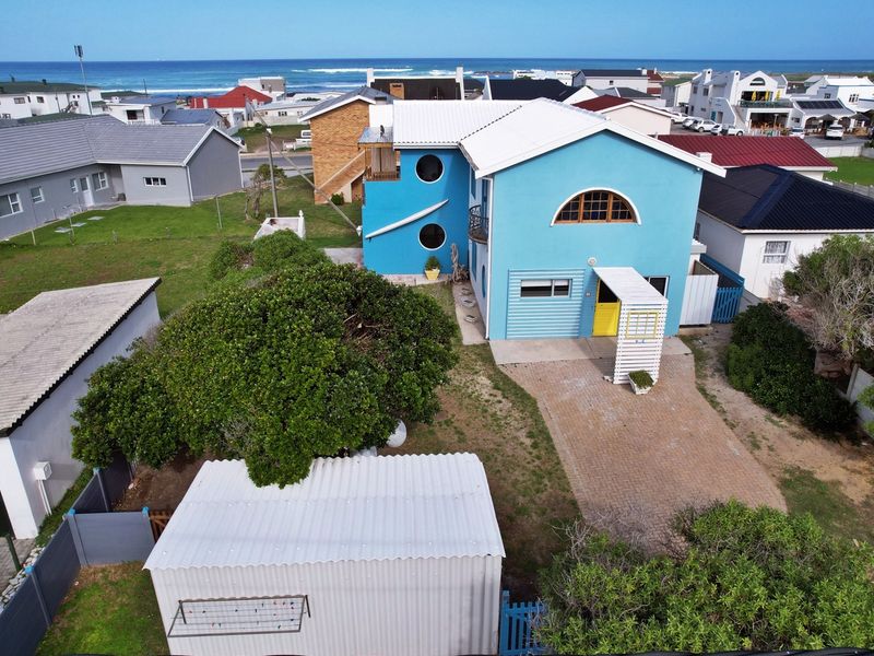 Aerial view of a blue coastal house featuring a metal roof, paved driveway, and a detached corrugated metal shed in the yard.