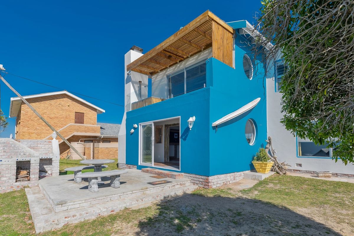 Rear exterior view featuring a blue facade, timber pergola, glass sliding doors, a brick patio, and a built-in outdoor braai area.