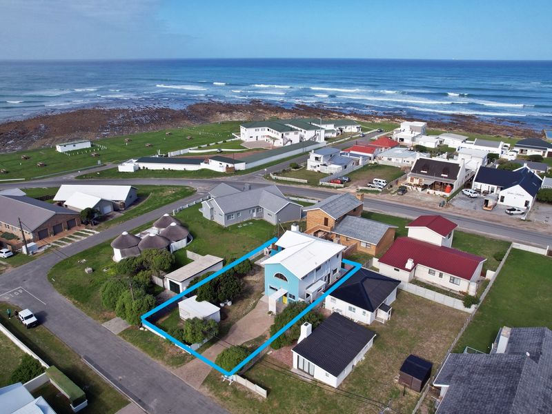 Aerial view of the property highlighting the building footprint, roof structure, driveway, and surrounding coastal neighborhood context.