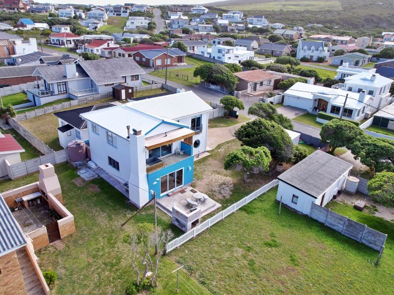 Aerial view of a residential property featuring a white house with a blue accent wall, a rear patio with a built-in braai, and a detached garage.