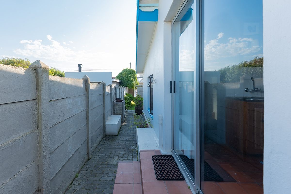 A narrow side passage featuring a paved walkway, precast concrete boundary wall, and access to the interior via a sliding glass door.