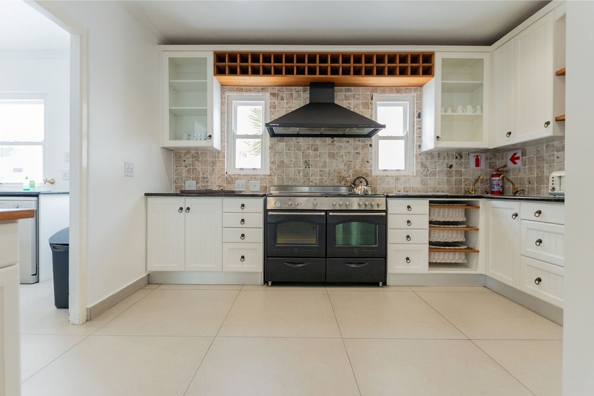 A well-maintained kitchen featuring white cabinetry, a black double oven with extractor fan, stone countertops, and a decorative tiled backsplash.