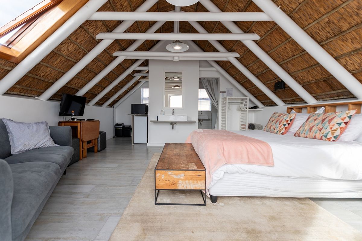 Spacious loft-style bedroom featuring exposed timber rafters, a thatched roof ceiling, skylight, and a modern wall-mounted basin area.