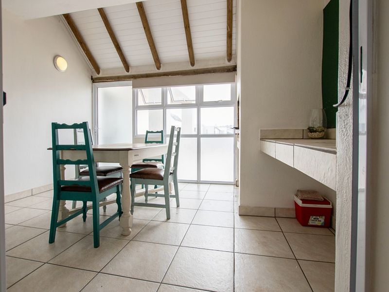 A bright, covered patio area featuring exposed timber ceiling beams, tiled flooring, and a built-in stone counter, ideal for outdoor dining and entertaining.