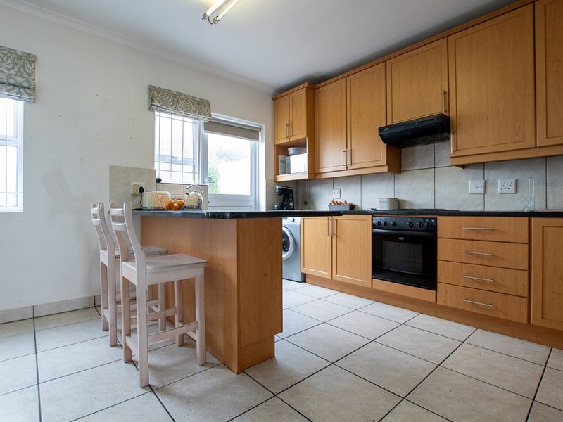 A functional kitchen featuring light wood cabinetry, granite countertops, built-in oven, hob, and tiled flooring with a breakfast bar area.