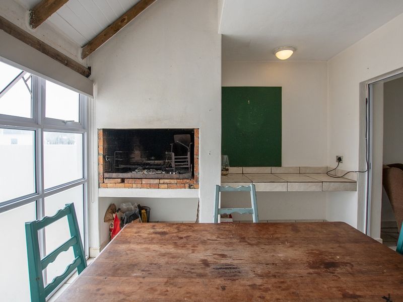 Enclosed patio area featuring a built-in braai, tiled prep surface, and exposed timber rafters, offering a functional space for indoor-outdoor entertaining.