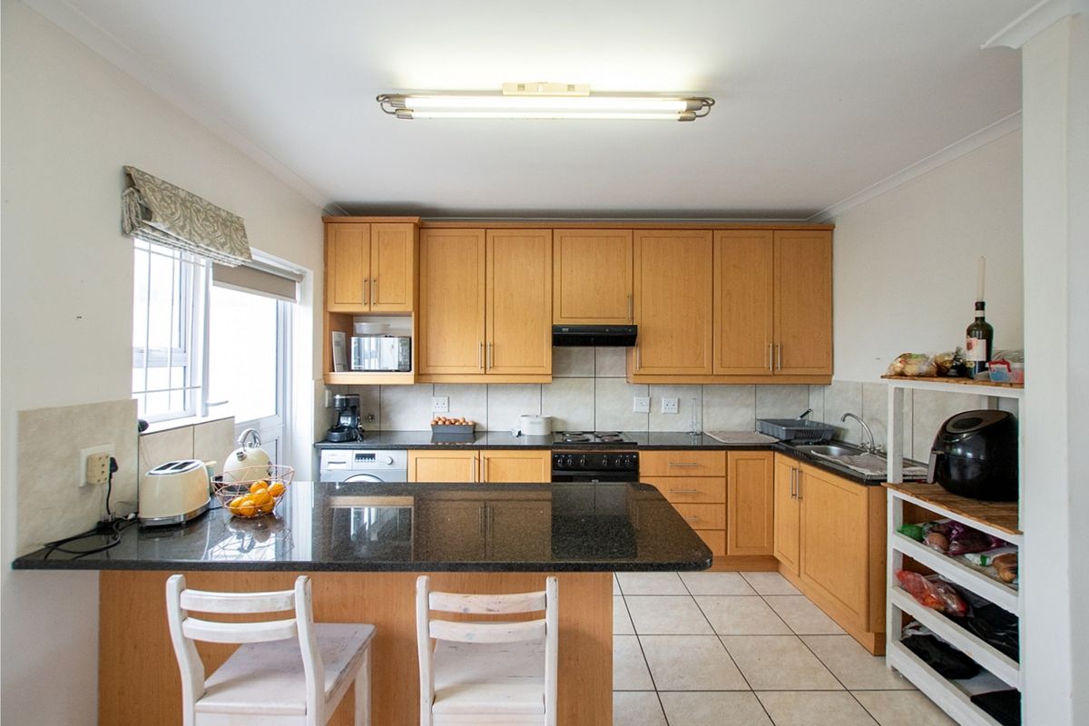 Functional kitchen featuring wooden cabinetry, granite countertops, a gas hob, and tiled flooring with a breakfast counter extension.