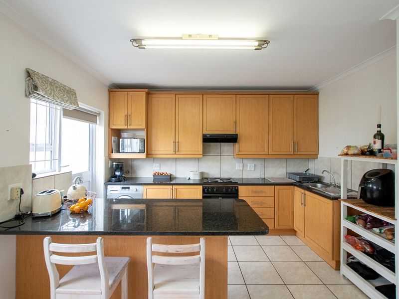 Functional kitchen featuring wooden cabinetry, granite countertops, a gas hob, and tiled flooring with a breakfast counter extension.