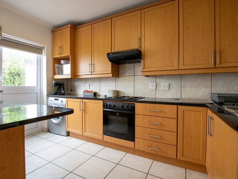A functional kitchen featuring wooden cabinetry, granite countertops, built-in oven, hob, extractor fan, and tiled flooring with direct access to the exterior.