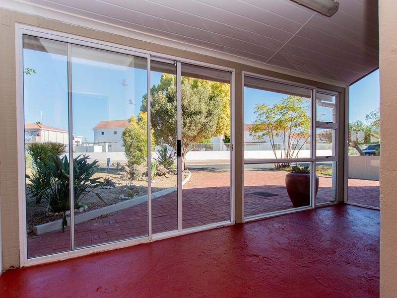 A covered patio area featuring sliding glass doors, a painted concrete floor, and a panelled ceiling, offering views of the front garden.