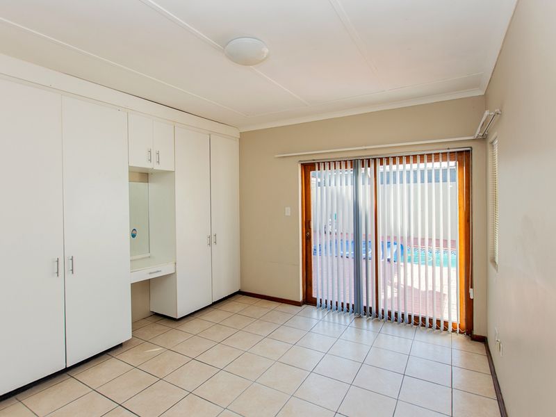 A bright bedroom featuring built-in cupboards with an integrated vanity, tiled flooring, and a sliding glass door providing access to the pool area.